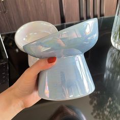 a hand holding a plastic cup on top of a black table next to a vase