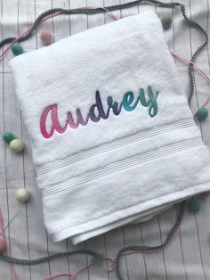 a white towel with the word audrey on it sitting on top of a bed covered in beads