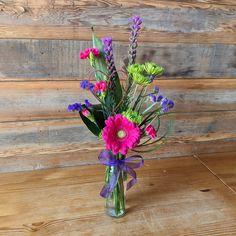 a vase filled with purple and green flowers on top of a wooden table next to a wall