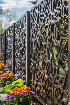 an iron fence with flowers in the foreground and trees in the backgroud