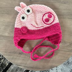 a pink and white crocheted hat on top of a wooden table next to a gray rug