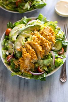 two plates filled with salad and dressing on top of a wooden table next to silverware