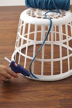 a person is knitting yarn on top of a white wire basket with blue thread and crochet hooks