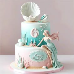 a birthday cake with a mermaid on top and seashells in the background,