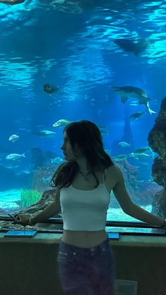 a woman standing in front of an aquarium looking at fish