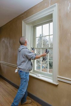 a man is painting the walls of a room with paint rollers and a window