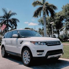 the white range rover is parked in front of some palm trees and an american flag