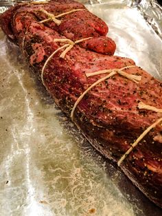 a large piece of meat wrapped in rope on top of aluminum foil with other food items around it