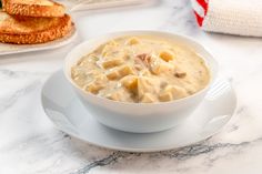 a white bowl filled with soup on top of a plate next to some toasted bread