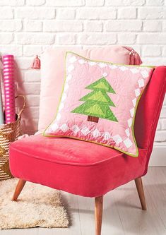 a pink chair with a christmas tree pillow on it next to a white brick wall