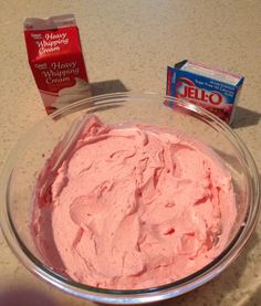 a glass bowl filled with pink frosting next to a carton of jello