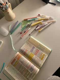 there are many different colored pencils on the table next to an open book and computer mouse