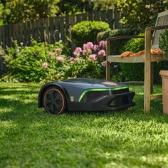 an electric lawn mower sitting in the grass next to a chair and potted plant