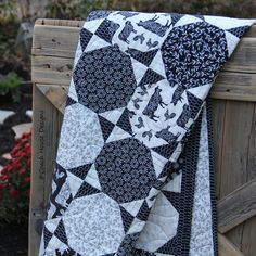 a black and white quilt is hanging on a wooden fence post with flowers in the background