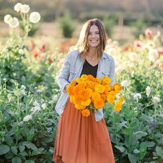 a woman in an orange skirt holding a bouquet of flowers and smiling at the camera