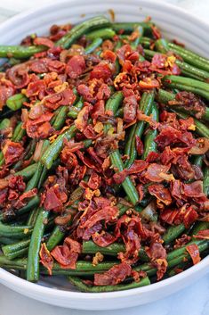 a white bowl filled with green beans covered in bacon and seasoning sitting on top of a table