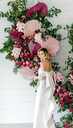 a woman in a white dress standing next to pink flowers and umbrellas on the wall