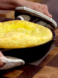 a person holding a skillet on top of a wooden table