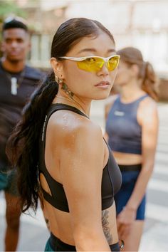 a woman wearing yellow sunglasses standing next to two other people on the street in front of her