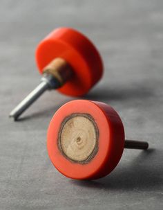 two red wooden knobs with holes in them on a gray surface and one has a screwdriver