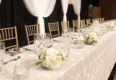 a long table with white flowers and silverware on it is set up for a formal function