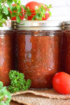 three jars filled with tomato sauce next to tomatoes and parsley