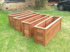 three wooden planters sitting in the grass near a car parked on the side of the road