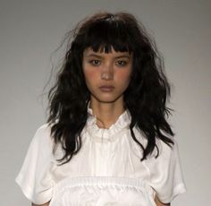 a woman with long black hair wearing a white shirt and skirt on the runway at london fashion week