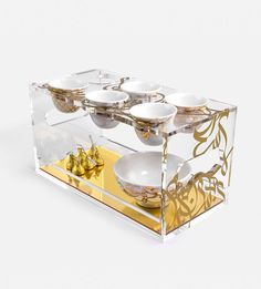 a clear box with gold and white dishes in it's display case on a white surface