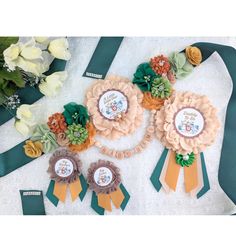 three ribbons with flowers on them sitting next to some other ribbon and flower decorations in the background