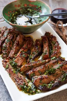 grilled steaks on a white platter with a bowl of sauce