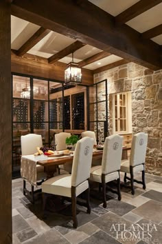 the dining room table is surrounded by white chairs and wooden beams with glass doors leading to an indoor wine cellar