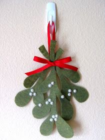 an ornament hanging on the wall decorated with green leaves and red ribbon bows