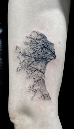 a woman's head and branches tattoo on the left side of her right arm