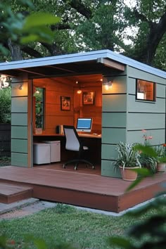 Small green backyard office with open door, lit interior, and desk with a computer. Minimal Backyard, Office Shed Ideas, Office She Shed, Outdoor Workspace, Dock Bar, Home Office Shed, Backyard Office Shed, Garden Office Shed, Farmhouse Sheds