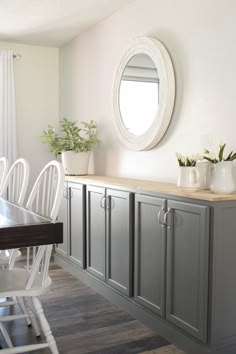 a dining room table with white chairs and gray cabinets