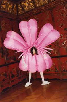 a woman standing in front of a large pink flower shaped object on top of a hard wood floor