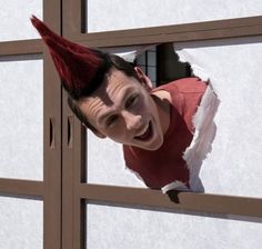 a man wearing a red shirt and elf hat looking through a hole in the wall