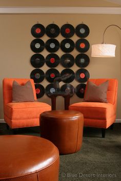 a living room with two orange chairs and a black record wall hanging on the wall