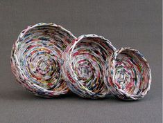 three baskets made out of newspaper are sitting side by side on a gray tablecloth