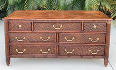 an old wooden dresser with many drawers and brass pulls on it's sides, in front of some palm trees