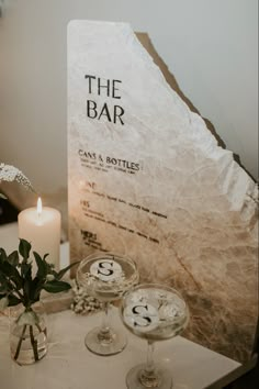 two wine glasses sitting on top of a table next to a sign that says the bar