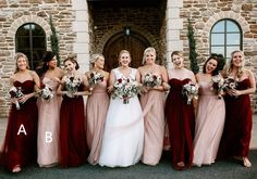 a group of women standing next to each other in front of a stone building holding bouquets