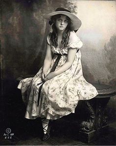 an old fashion photo of a woman in a dress and hat sitting on a bench