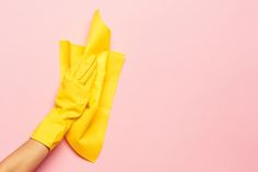 a person's hand in yellow rubber gloves on a pink background with cleaning supplies