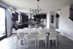 a dining room table with white chairs and balloons hanging from the ceiling in front of an open kitchen