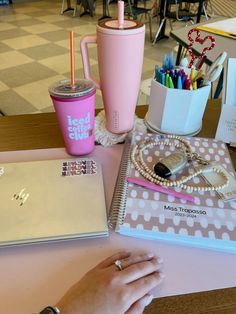 a person's hand on a desk next to a laptop, notebook and cup