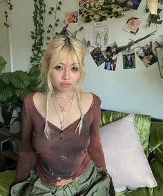 a woman sitting on top of a green couch next to a wall with pictures and plants