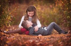 a young boy and girl cuddling on the ground in an autumn forest with leaves