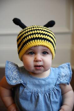 a small child wearing a yellow and black crochet bee hat on top of her head